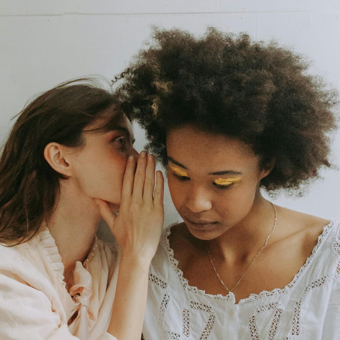 Twee vrouwen die in elkaars oor fluisteren. Illustratief beeld bij oproep voor verhalen waar je je voor schaamt