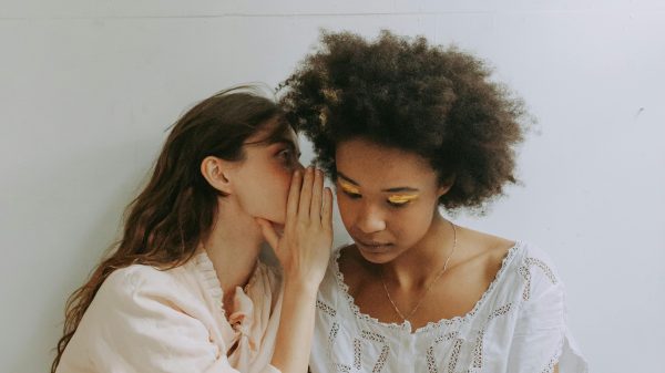 Twee vrouwen die in elkaars oor fluisteren. Illustratief beeld bij oproep voor verhalen waar je je voor schaamt