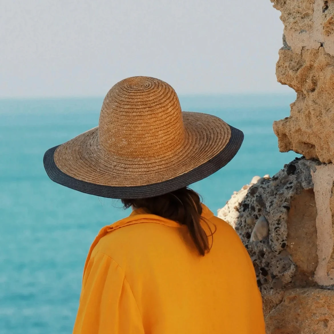 Oproep voor vakantie verhalen, illustratief beeld van een vrouw met een hoed op bij de zee