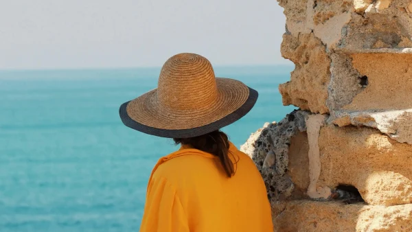 Oproep voor vakantie verhalen, illustratief beeld van een vrouw met een hoed op bij de zee