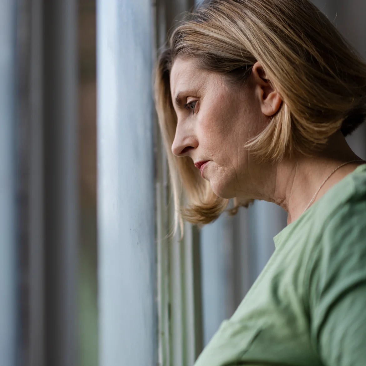 Vrouw staat voor het raam en denkt na over haar stiefmoeder die veel geld uitgeeft