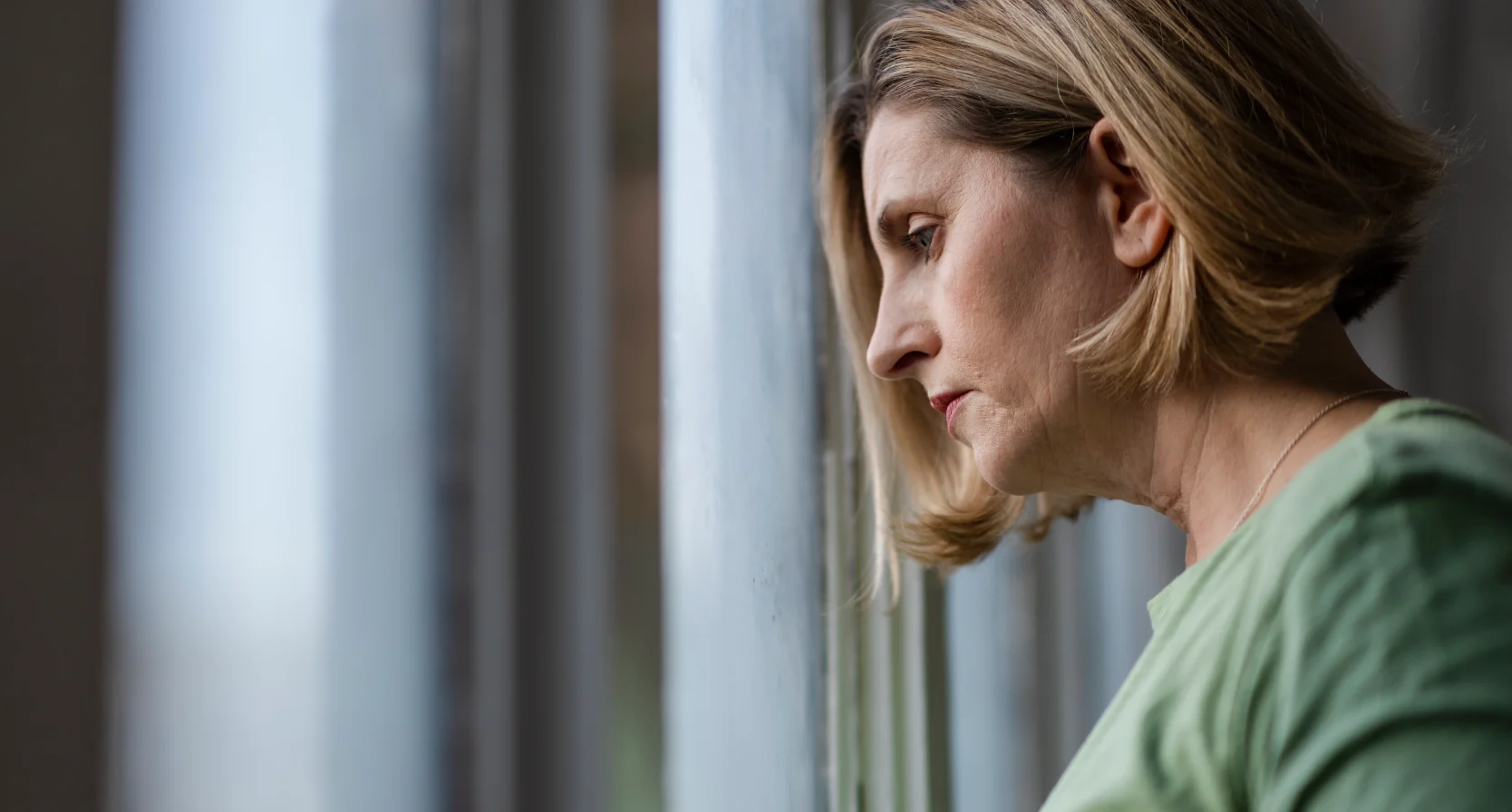 Vrouw staat voor het raam en denkt na over haar stiefmoeder die veel geld uitgeeft