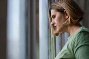 Vrouw staat voor het raam en denkt na over haar stiefmoeder die veel geld uitgeeft