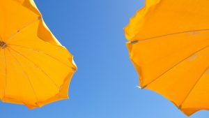 Tropische temperaturen dit weekend, illustratief beeld van twee parasols in de blauwe lucht