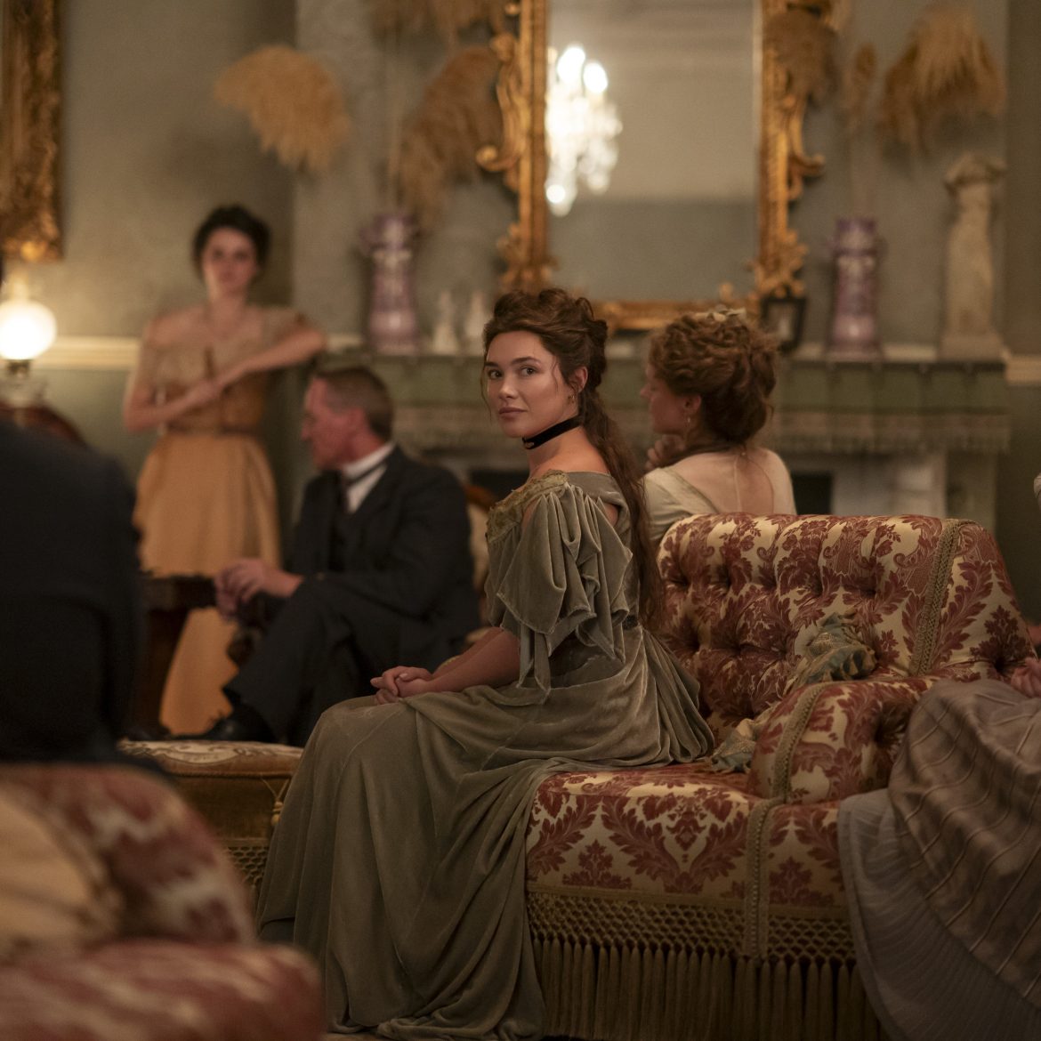 east of eden Netflix "A group of people in period clothing sit in an ornate, vintage living room with elegant furniture, antique decorations, and a large mirror above the fireplace, engaged in conversation or listening."
