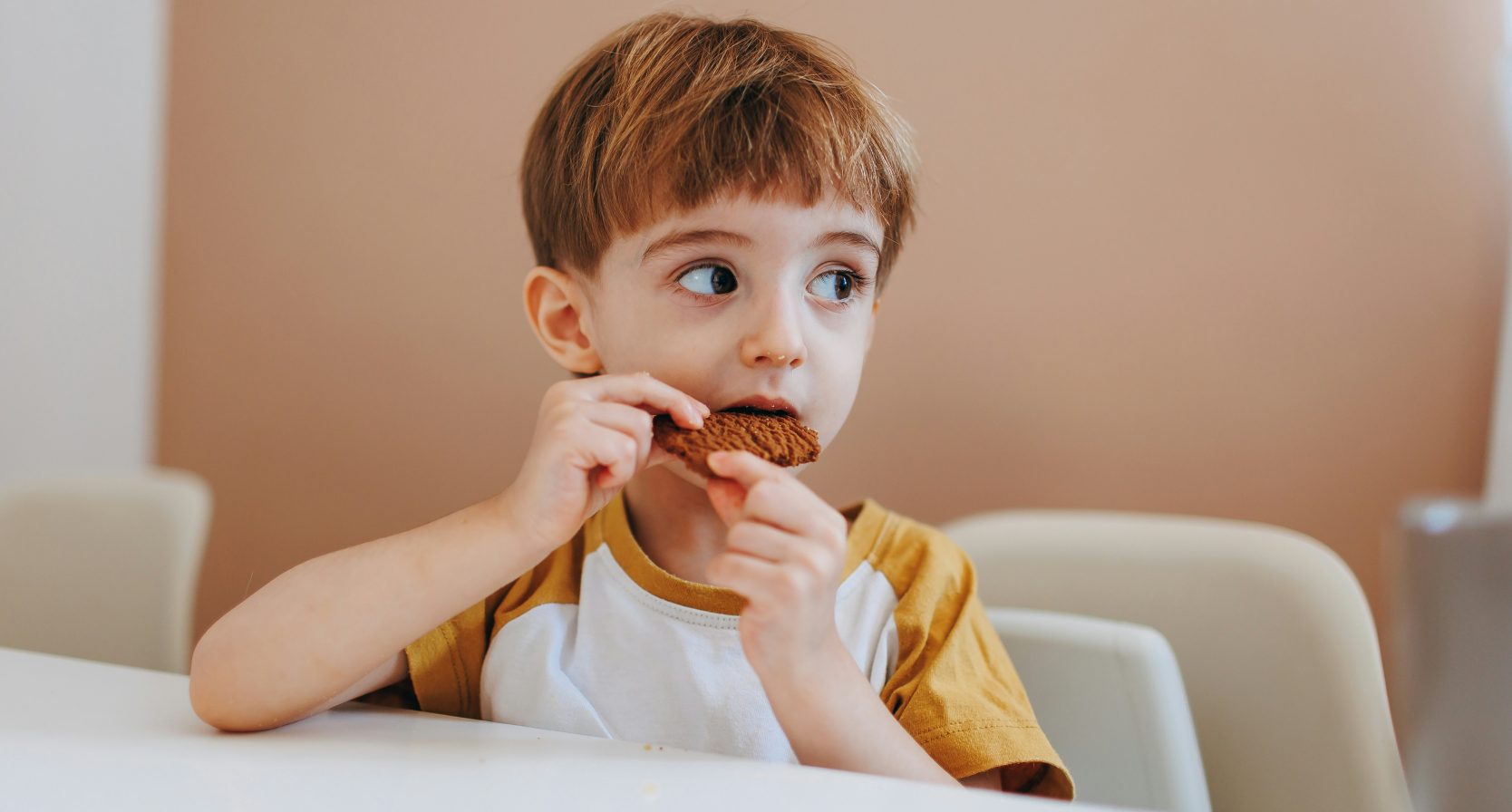 Jongen zit aan tafel en eet een koekje