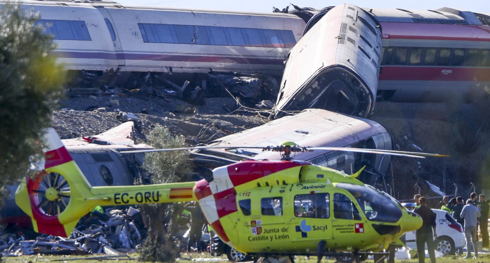 Een traumahelicopter staat op de plek des onheils klaar. Op de achtergrond zie je de ontspoorde treinstellen.